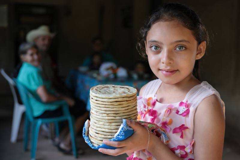 niña sostiene una torre de tortillas de maíz