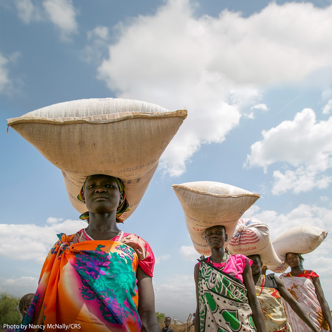Women carrying large bages of rice on their heads.
